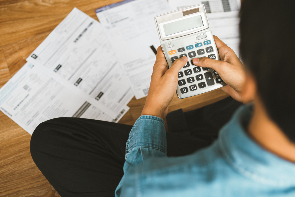 whats-happening-in-the-energy-market1887657550.png man sitting on floor with bills and using a calculator
